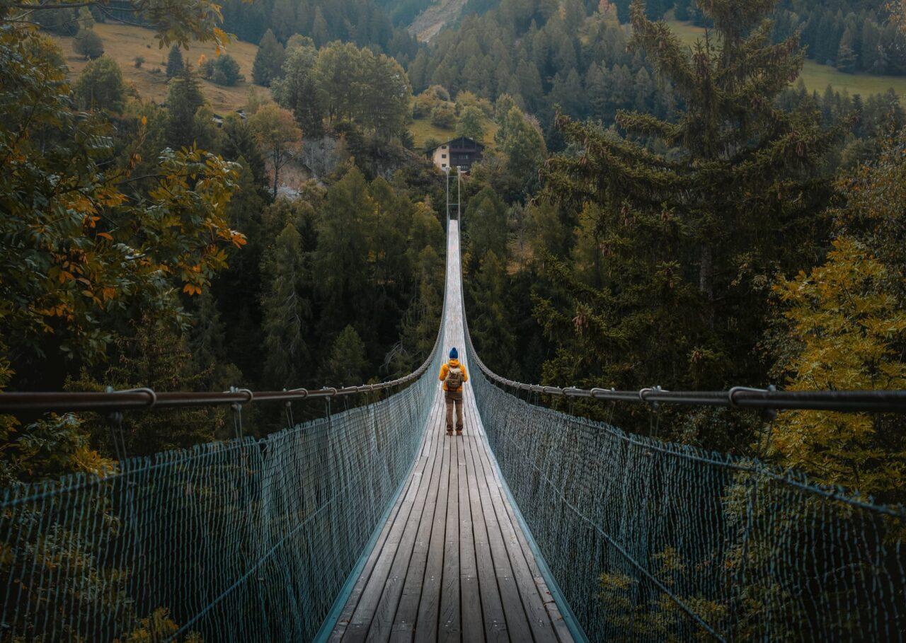 Man standing on a suspension bridge over a deep gorge